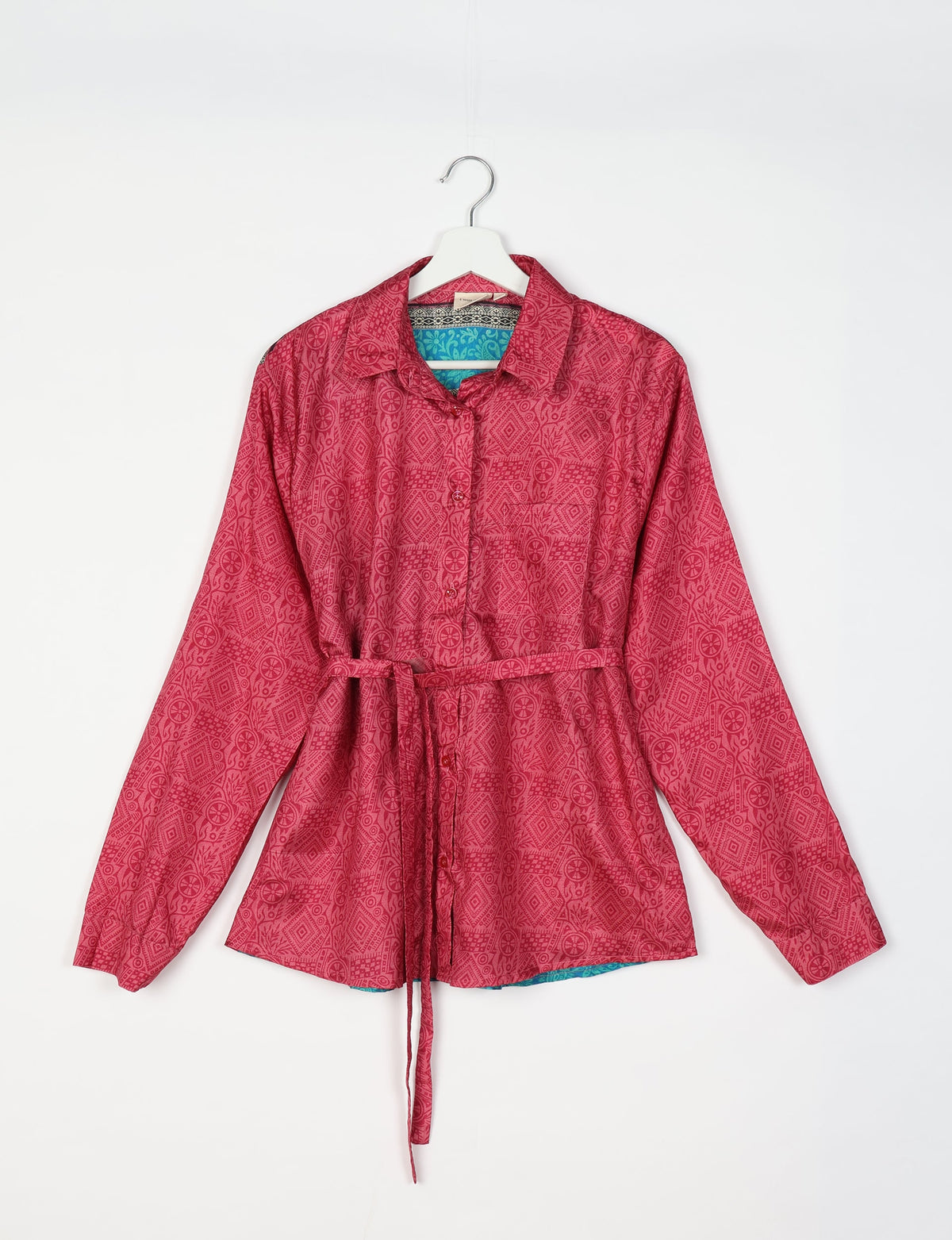 Pink long-sleeve button-up shirt with tropical geometric print, collar, and waist tie, shown hanging on white hanger