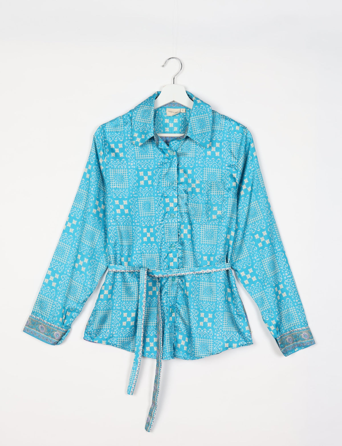 Blue Indian ethnic shirt with white geometric patterns, long sleeves, collar, and a matching fabric belt, hanging on a white hanger