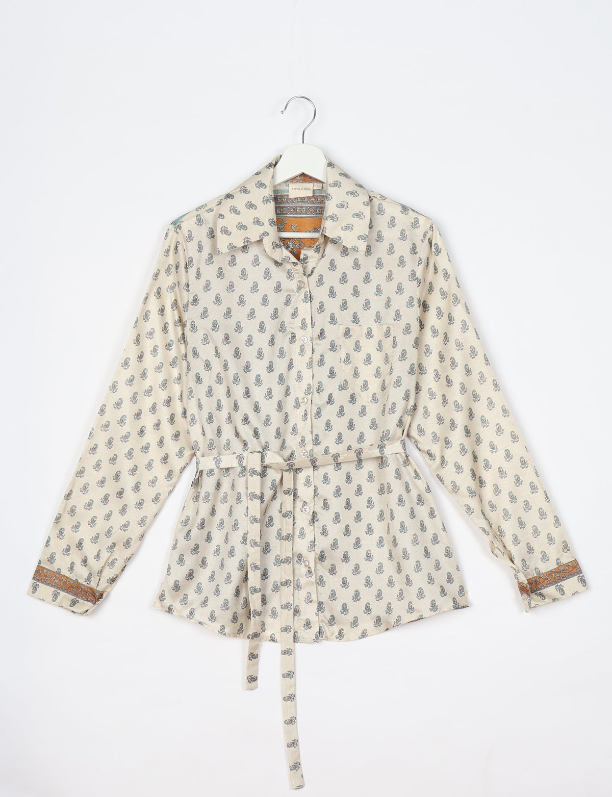 Long-sleeve beige shirt with small blue floral print, button front, collar, belt, and orange patterned cuffs, hanging flat