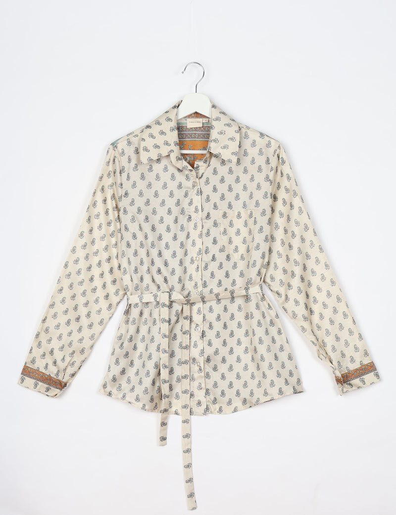 Long-sleeve beige shirt with small blue floral print, button front, collar, belt, and orange patterned cuffs, hanging flat