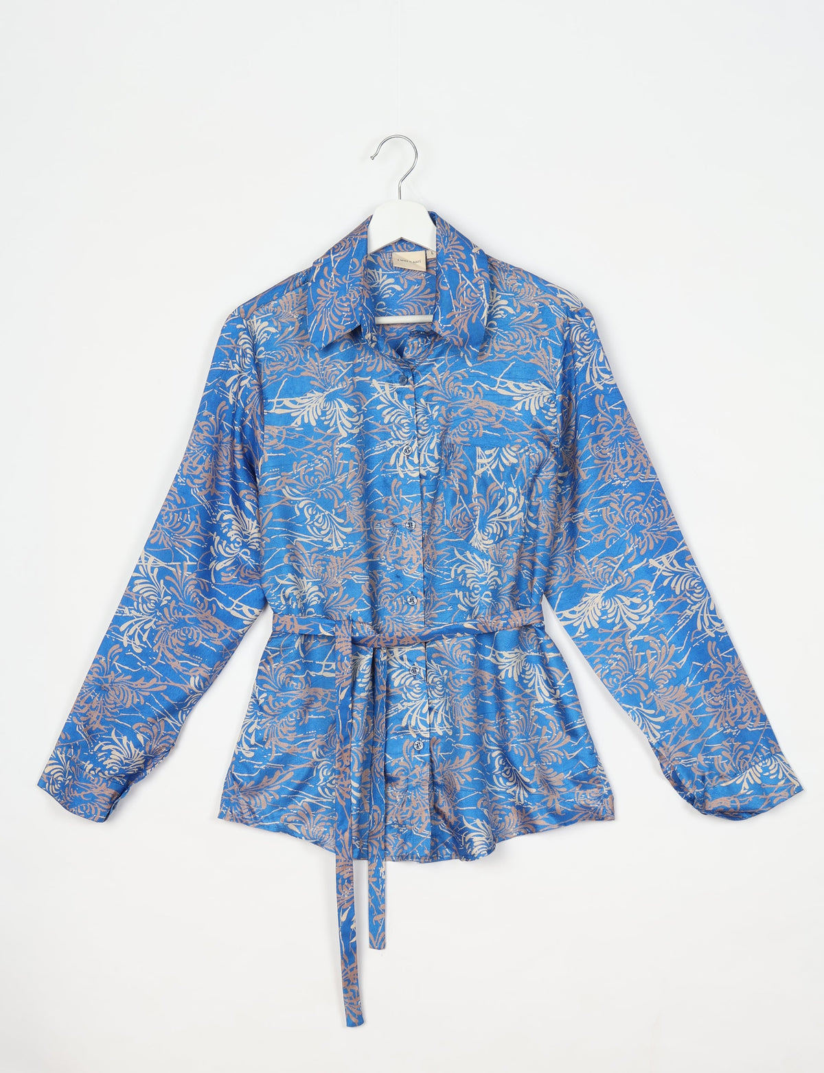 Blue long-sleeve shirt with abstract beige floral pattern, button front, collar, and waist tie, hanging on white hanger