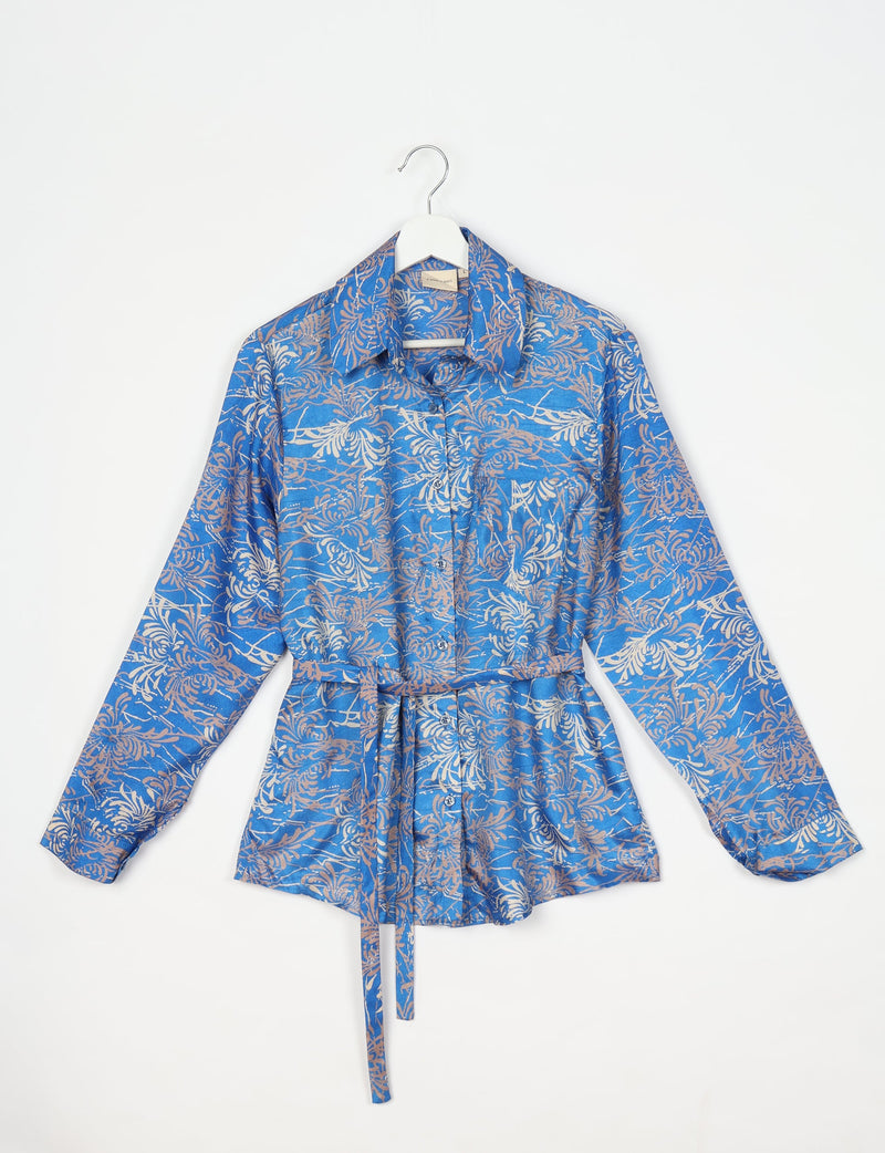 Blue long-sleeve shirt with abstract beige floral pattern, button front, collar, and waist tie, hanging on white hanger
