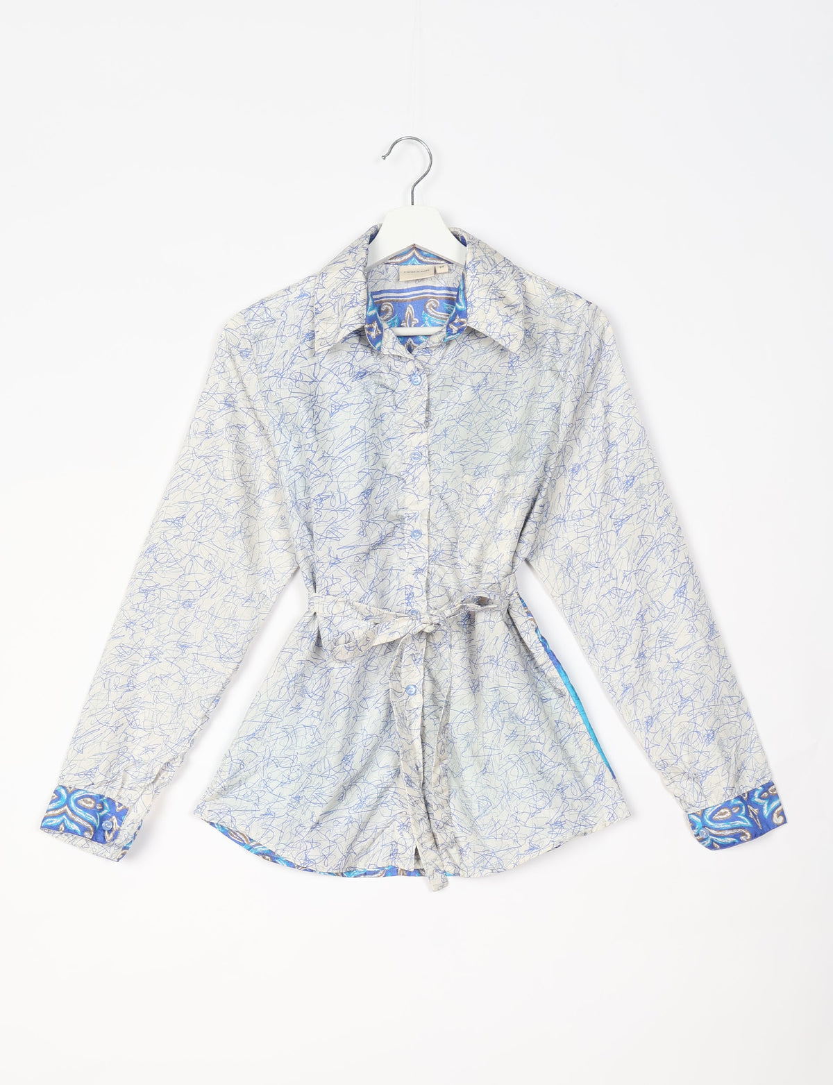 White long-sleeve button-up shirt with blue abstract scribble pattern, blue paisley collar and cuffs, and waist tie, hanging flat