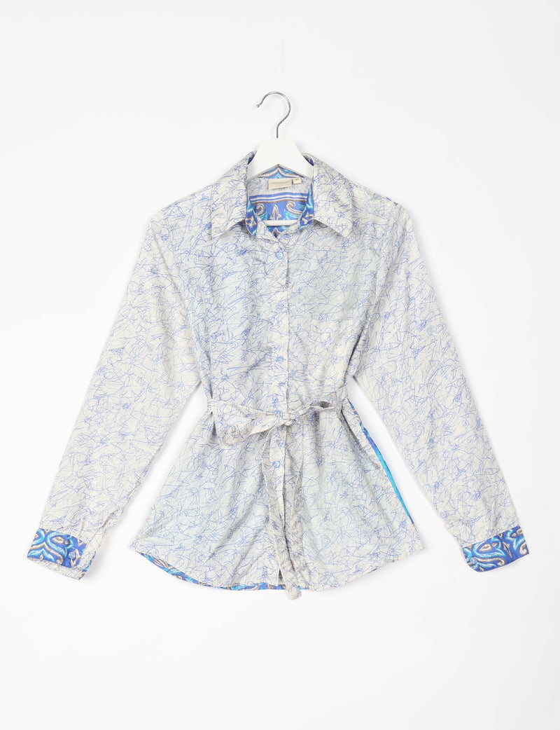 White long-sleeve button-up shirt with blue abstract scribble pattern, blue paisley collar and cuffs, and waist tie, hanging flat