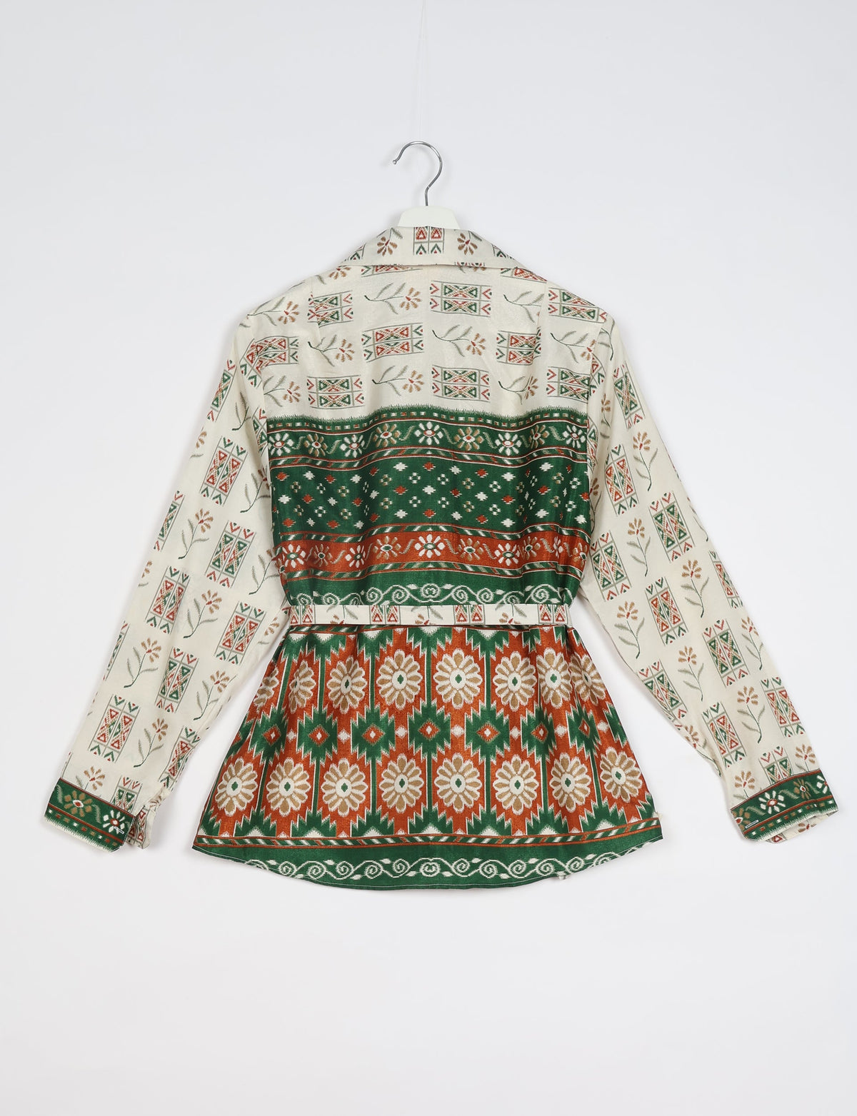 White ethnic shirt with green and rust geometric and floral patterns, long sleeves, and buttoned cuffs, back view on hanger