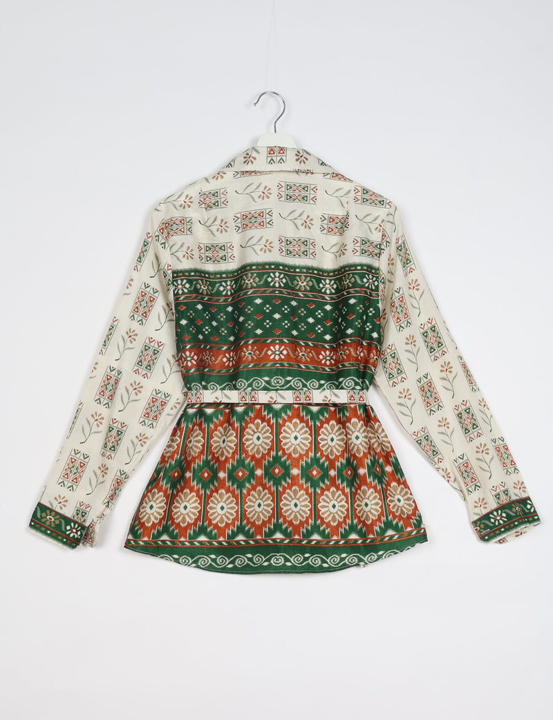 White ethnic shirt with green and rust geometric and floral patterns, long sleeves, and buttoned cuffs, back view on hanger