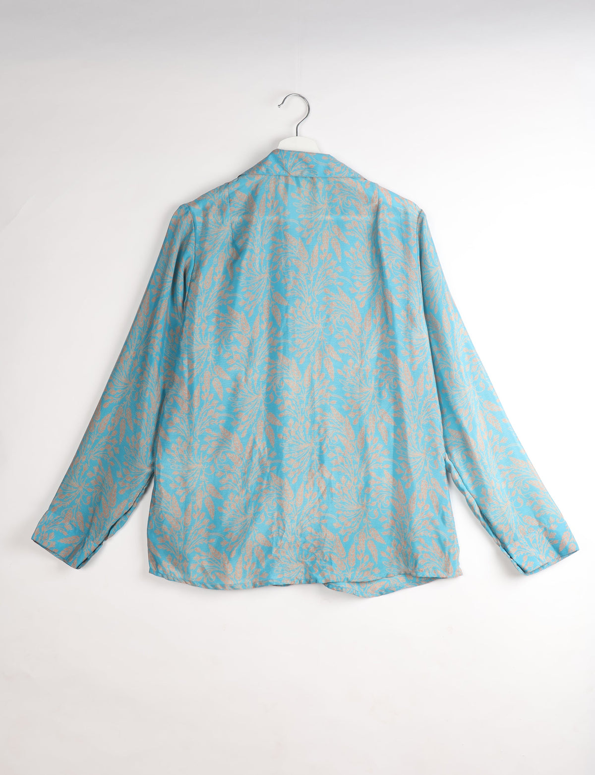 Blue long-sleeve shirt with beige tropical leaf pattern, shown from back, hanging on white hanger against white background