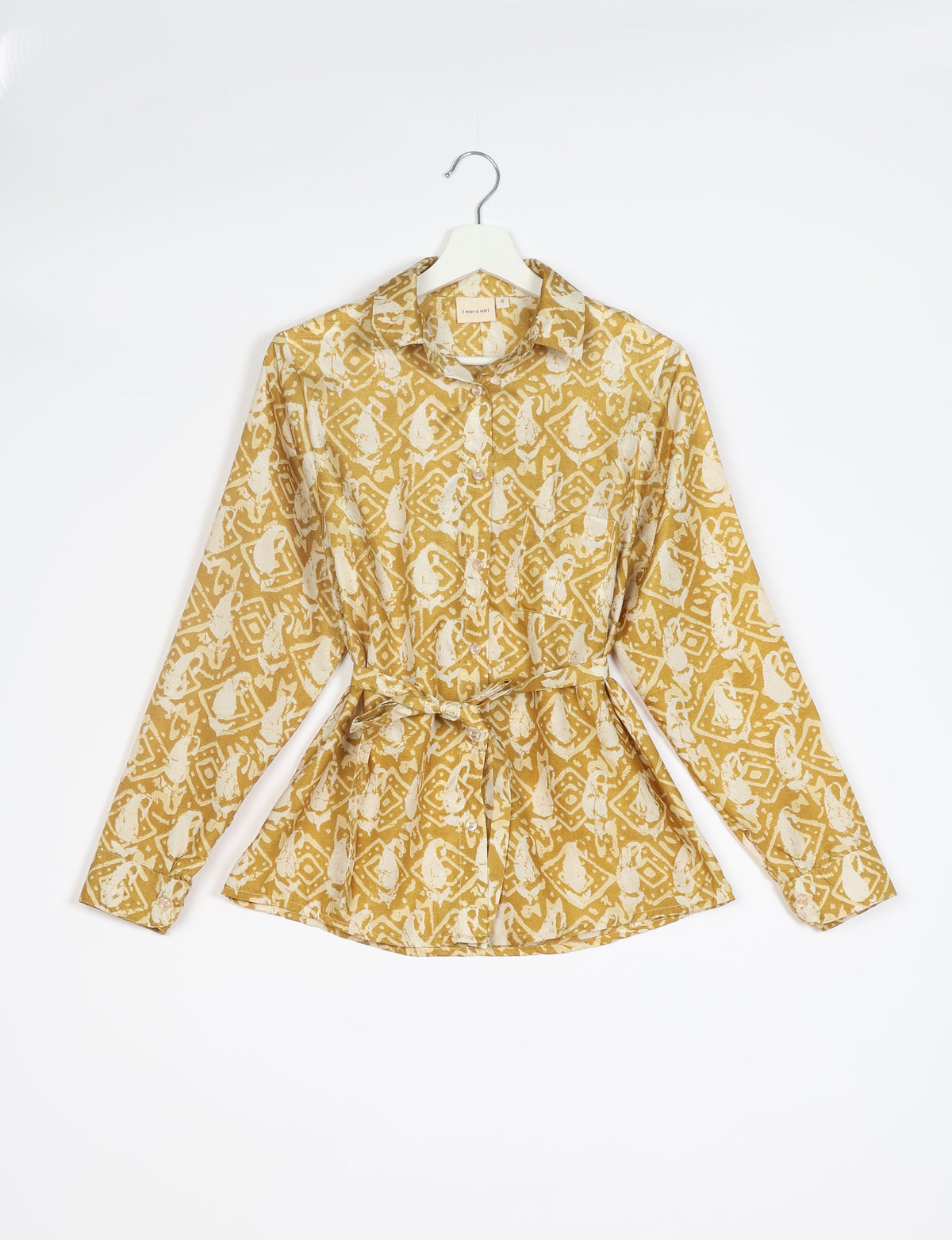 Long-sleeve button-up shirt with collar and belt, mustard yellow with white abstract tropical print, hanging on white hanger