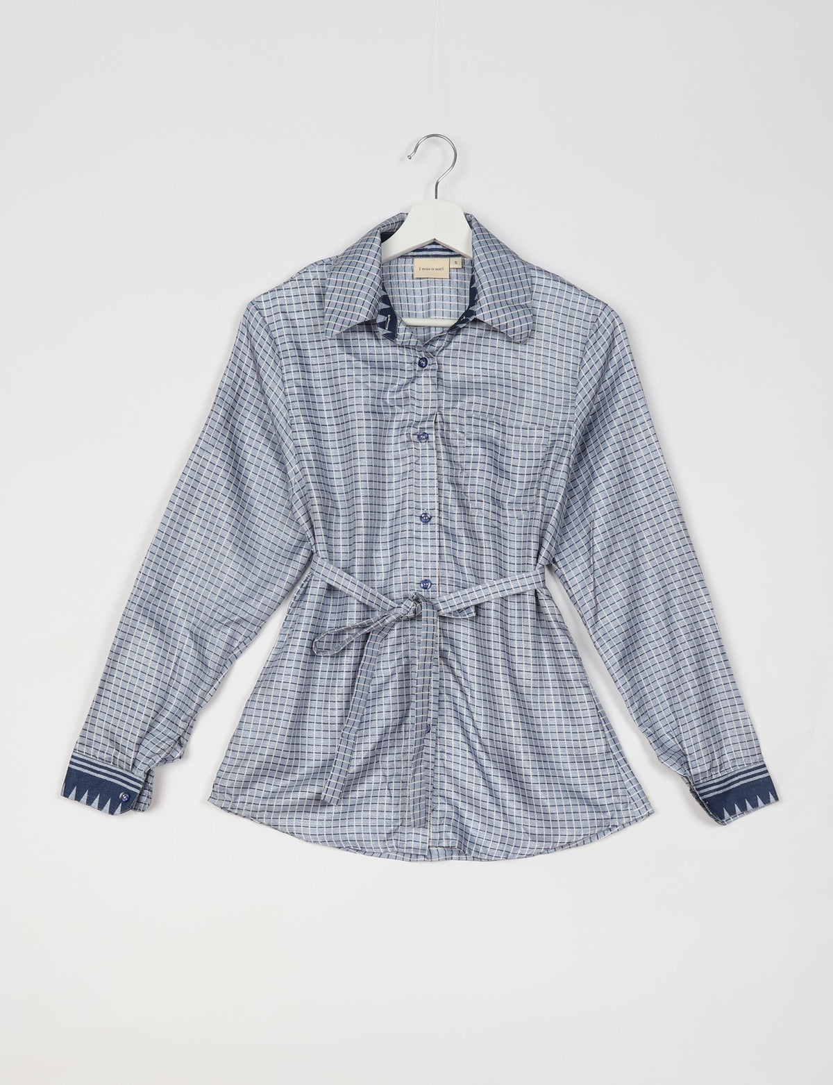 Grey button-up shirt with geometric grid pattern, long sleeves, tie belt, and contrasting dark blue cuffs, hanging on white hanger