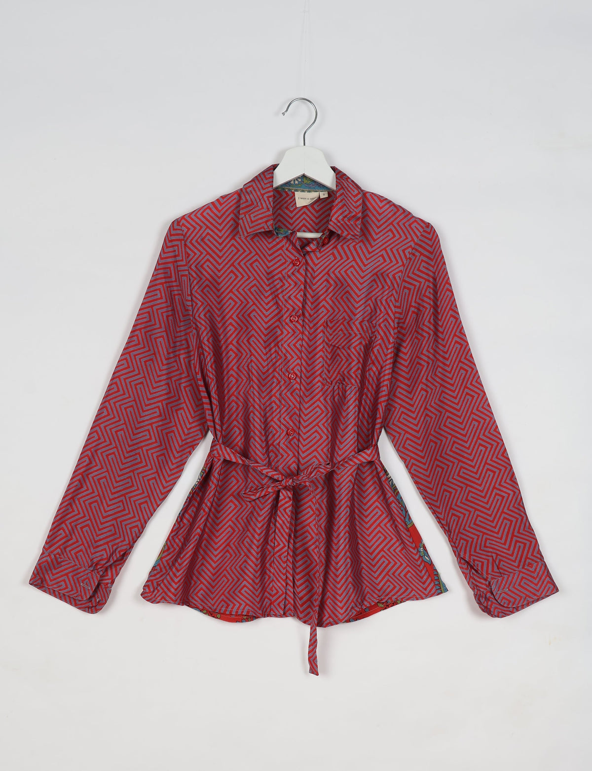Pink geometric patterned long-sleeve shirt with collar and waist tie, hanging on a white hanger against a white background