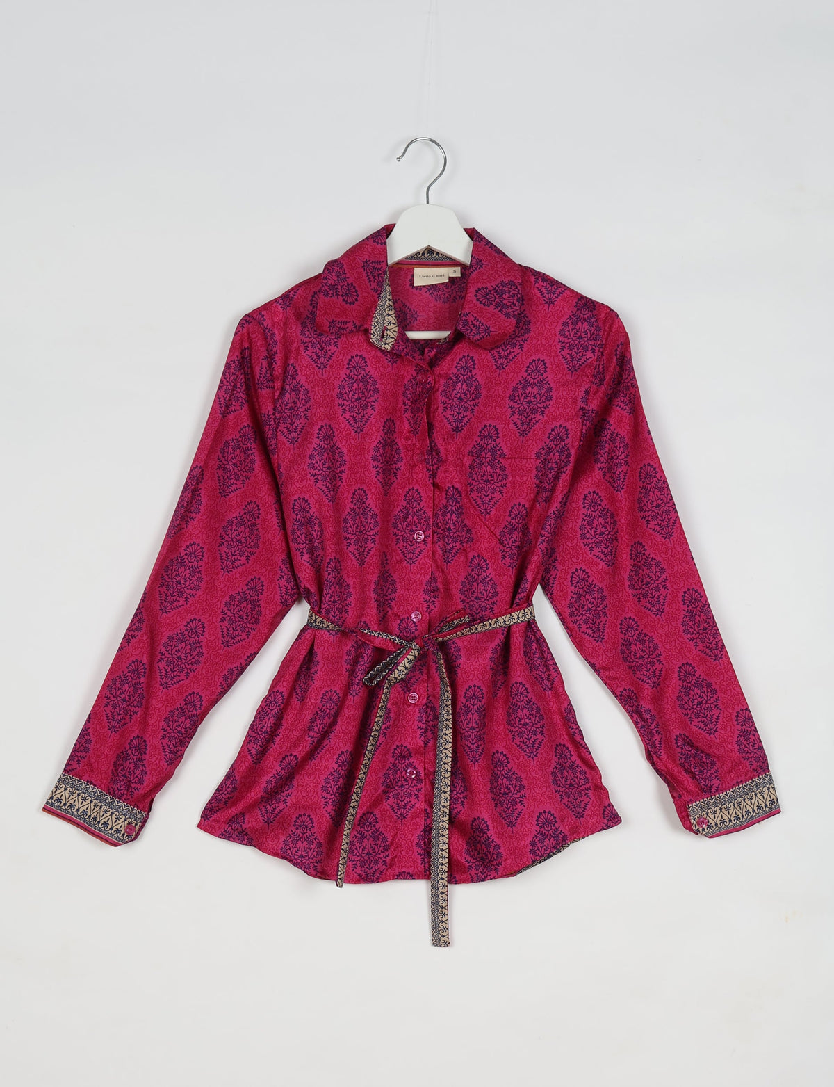 Pink Indian ethnic shirt with dark blue floral patterns, button front, long sleeves, and a patterned waist tie, hanging on a hanger