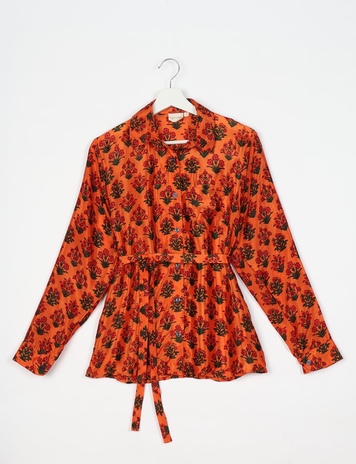 Orange long-sleeve button-up shirt with red and black floral print, collar, chest pocket, and waist tie, hanging on white hanger