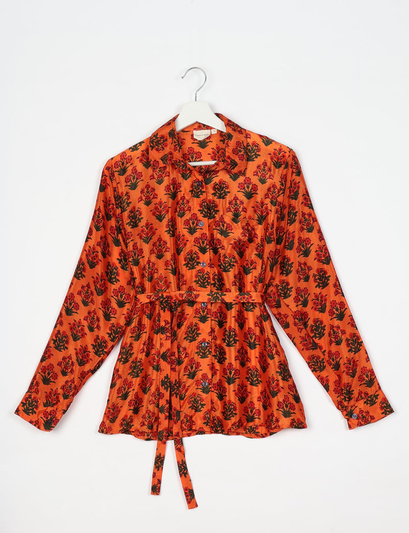Orange long-sleeve button-up shirt with red and black floral print, collar, chest pocket, and waist tie, hanging on white hanger