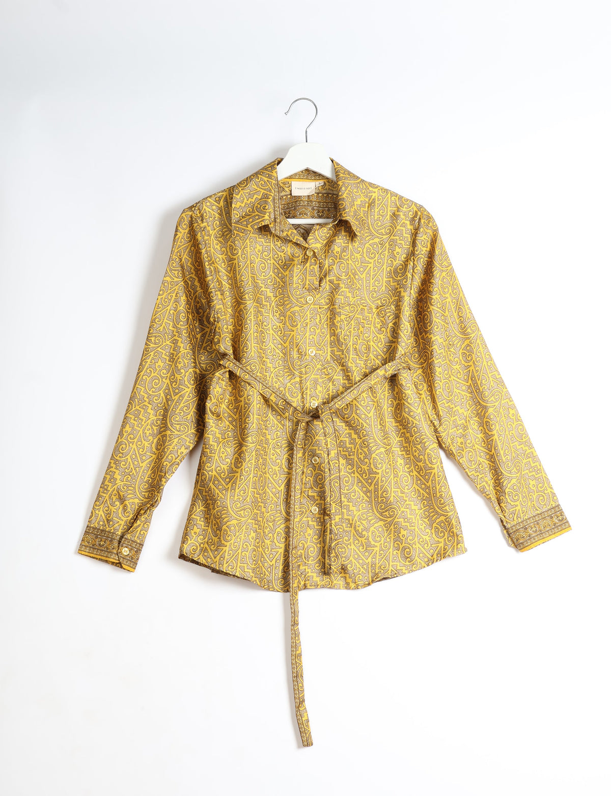 Yellow long-sleeve button-up shirt with intricate paisley pattern and waist tie, hanging on white hanger against white background