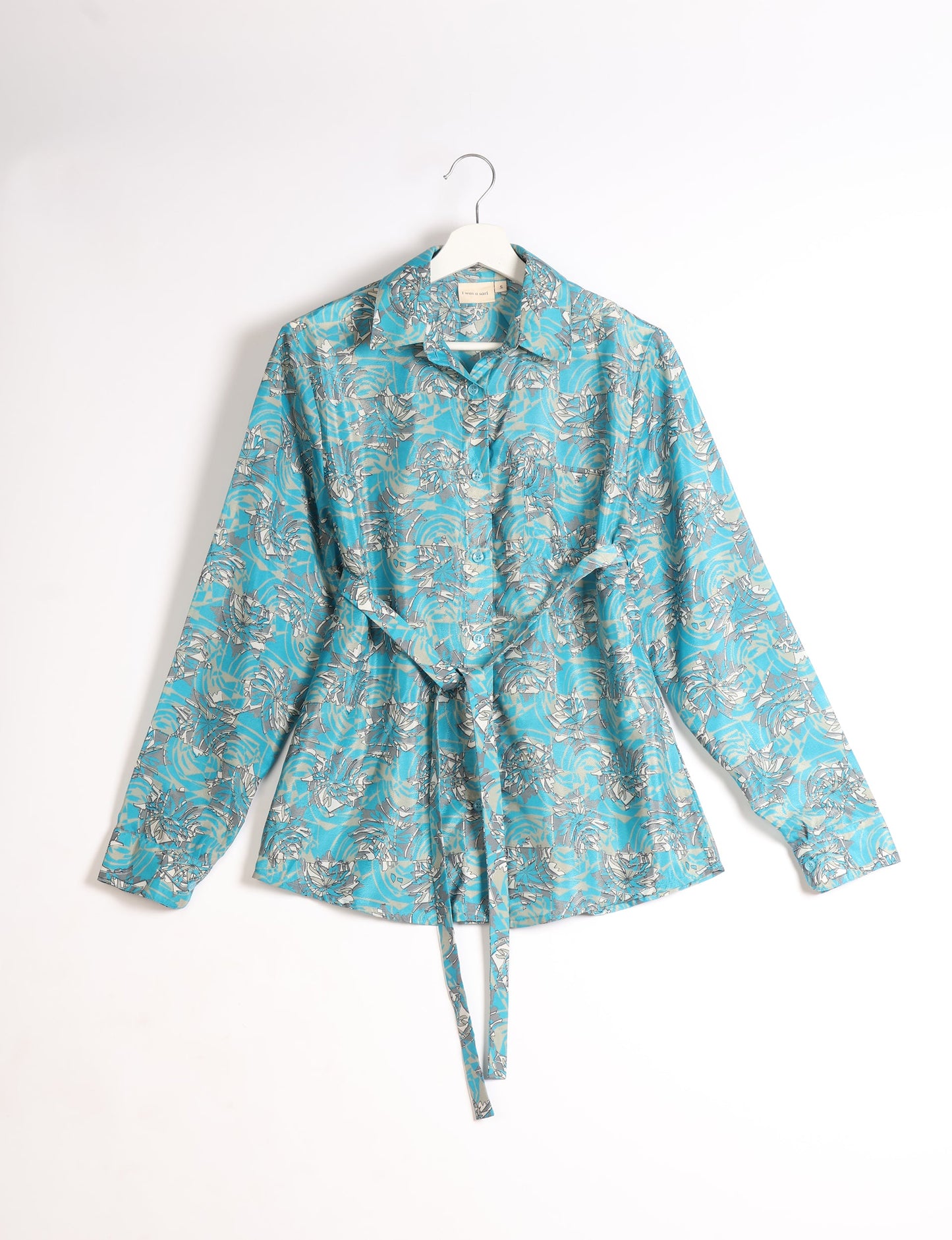 Experience sustainable fashion with our classic slim-fit shirt, crafted with ethical and green values. The shirt, designed for minimal waste, features a tie-up waist belt or neck tie, semi-spread collar, and regular shirt cuffs. Versatile and eco-friendly, wear it tucked in, unbuttoned over a tank top, or knotted at the waist for a unique style.