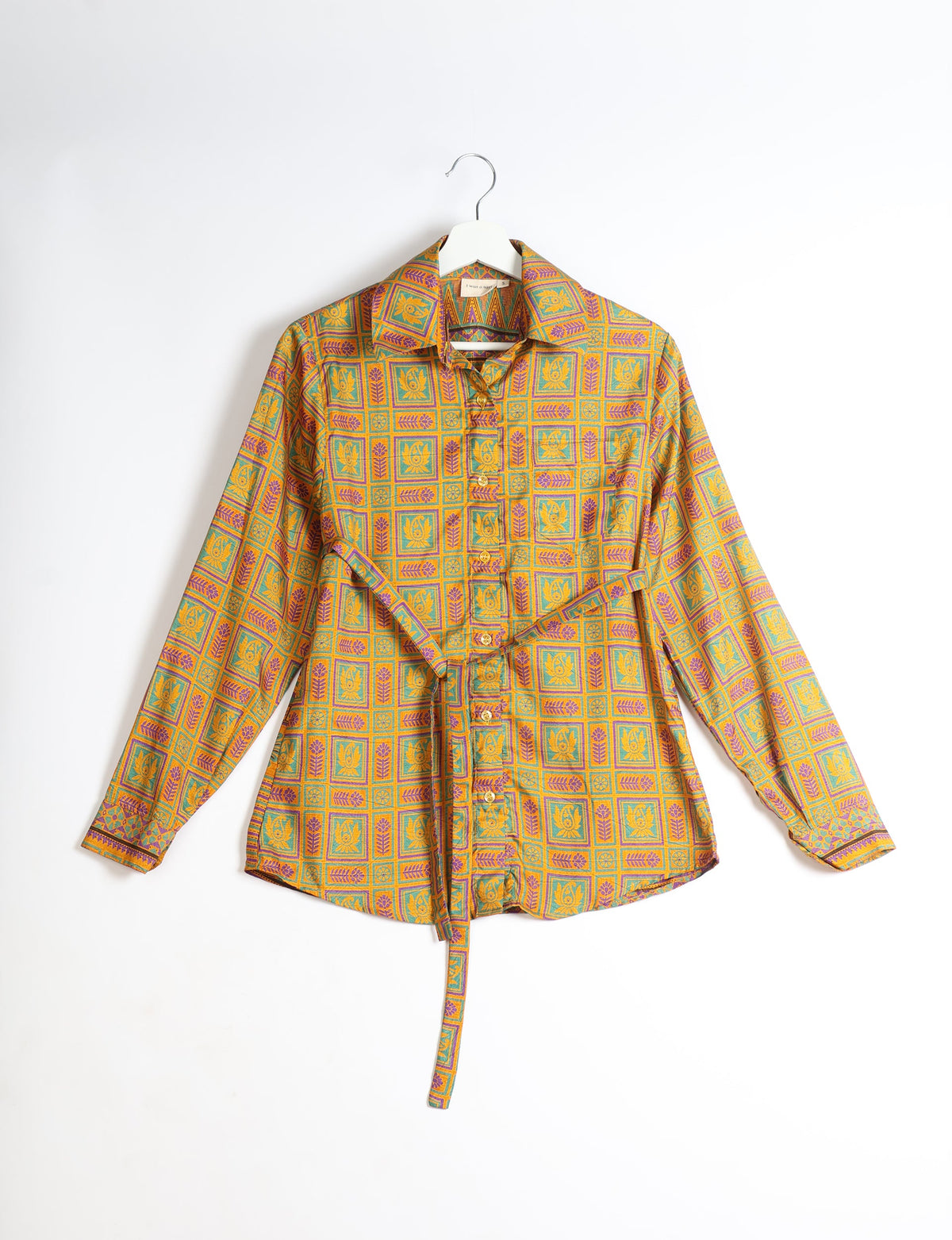Yellow long-sleeve button-up shirt with geometric floral pattern in green and purple, hanging on white hanger, front view