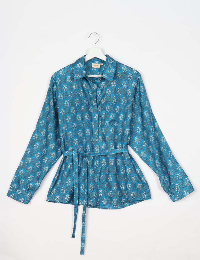Blue long-sleeve button-up shirt with white and black tropical pattern, collar, and waist tie, hanging on white hanger