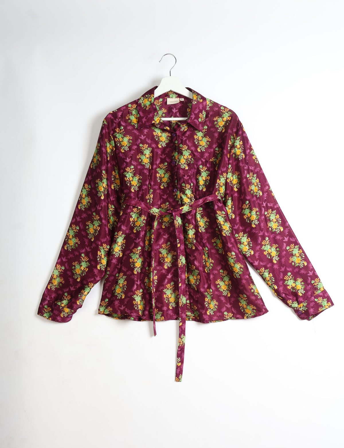 Purple long-sleeve button-up shirt with yellow and green floral print, collar, and waist tie, hanging on white hanger