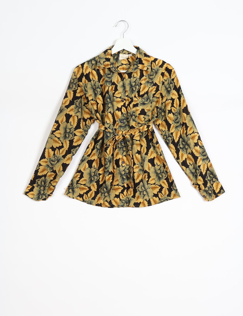 Long-sleeve button-up shirt with yellow and green leaf pattern on black background, tied waist, front pocket, on white hanger