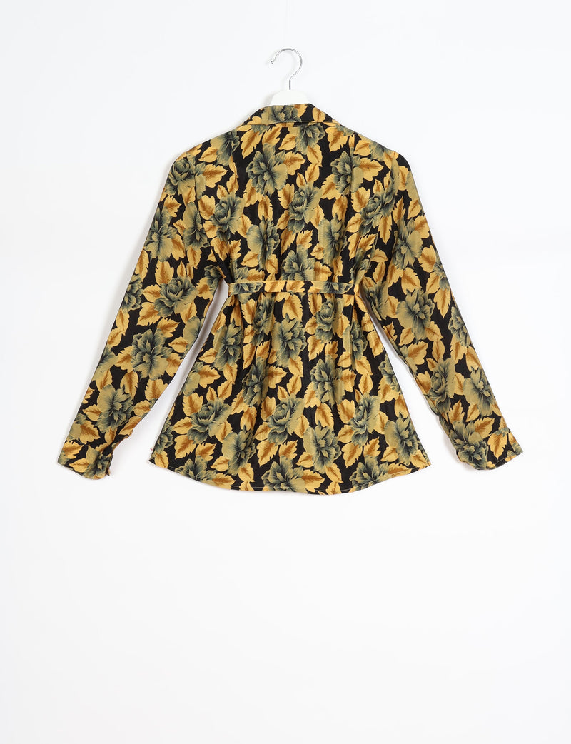 Long-sleeve shirt with yellow and green leaf floral pattern on black, back view, hanging on white hanger with belt detail