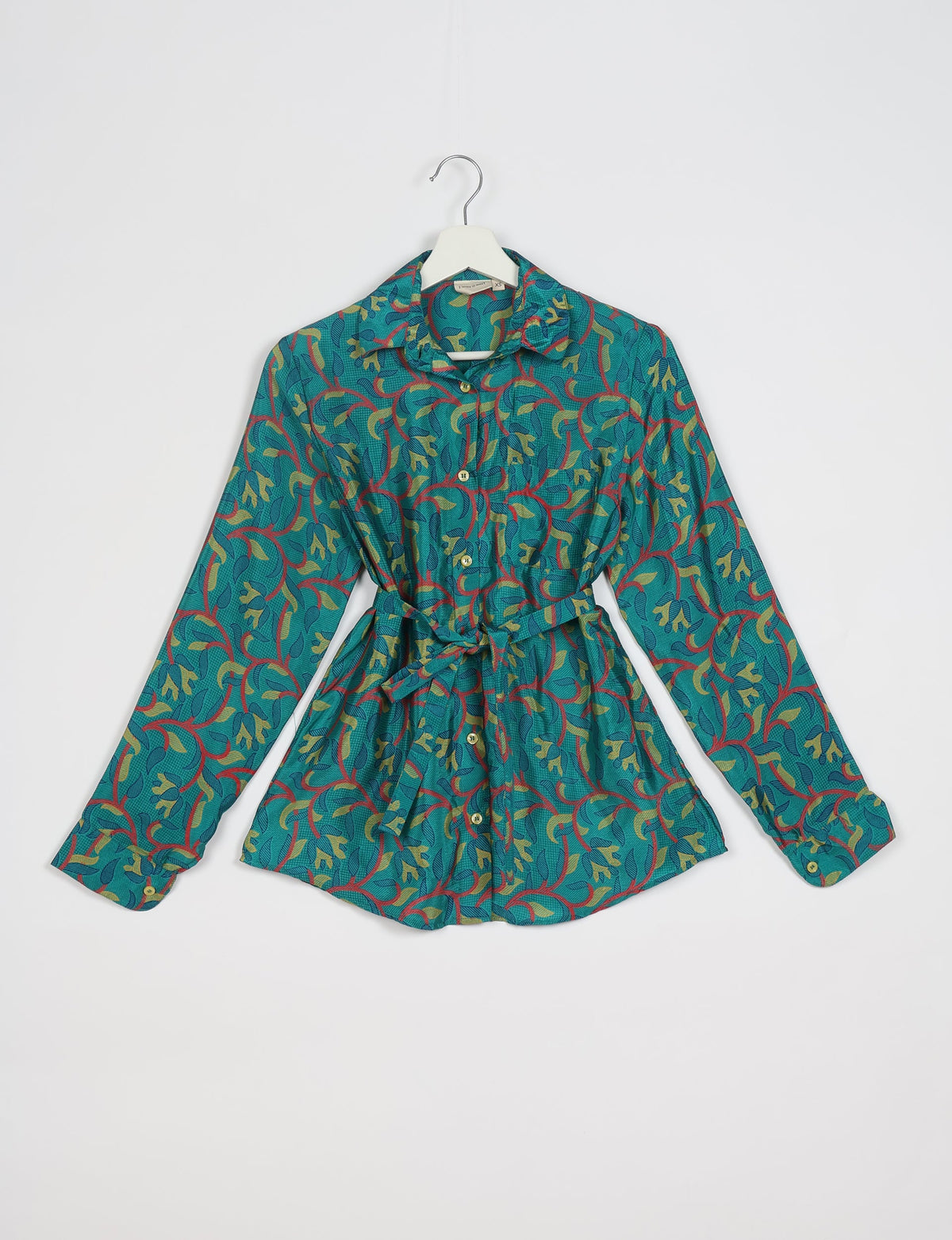 Blue long-sleeve button-up shirt with abstract green and red leaf pattern, collar, chest pocket, and waist tie, on hanger