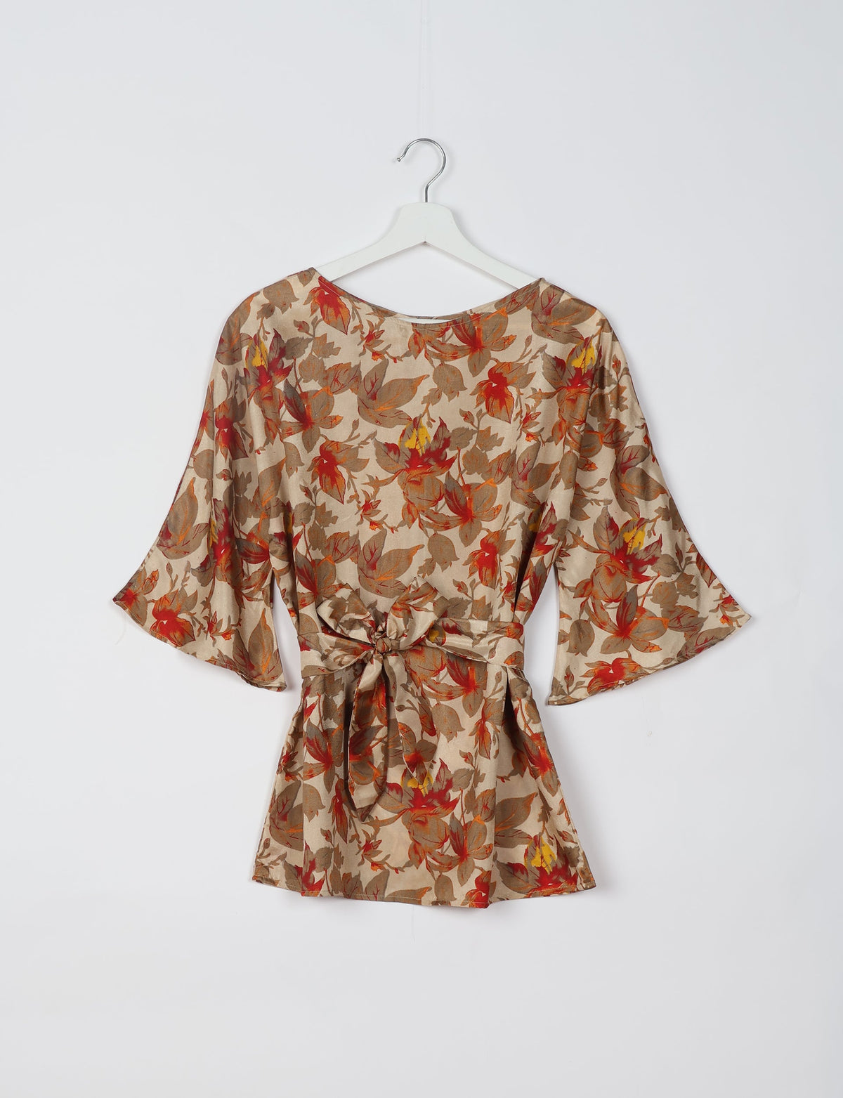 Beige floral belt top with red, orange, and yellow leaves, wide sleeves, and a tied waist, shown hanging on a white hanger