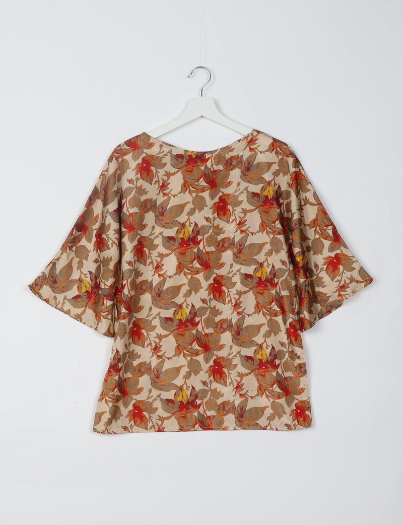 Beige top with red, brown, and yellow floral print, wide sleeves, and round neckline hanging on white hanger