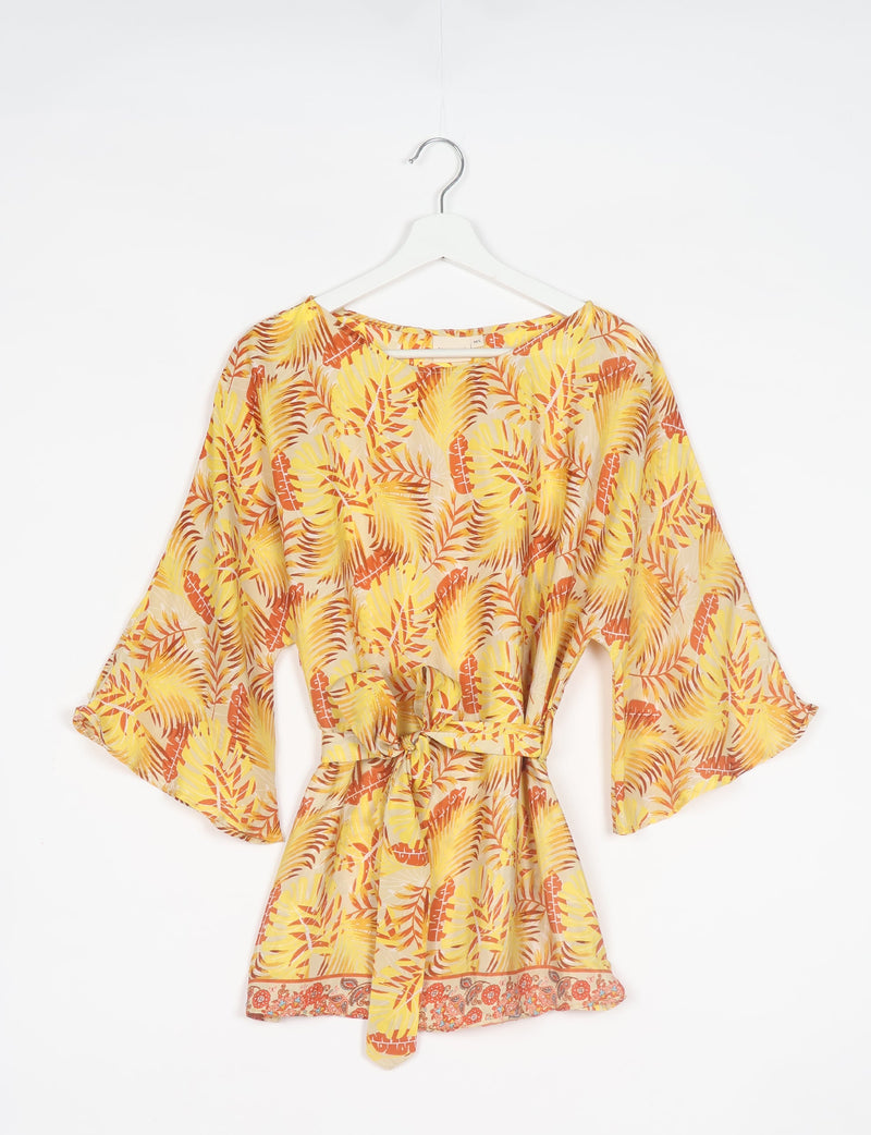 Yellow and orange leaf print belt top with wide sleeves and floral border hem, hanging on white hanger front view