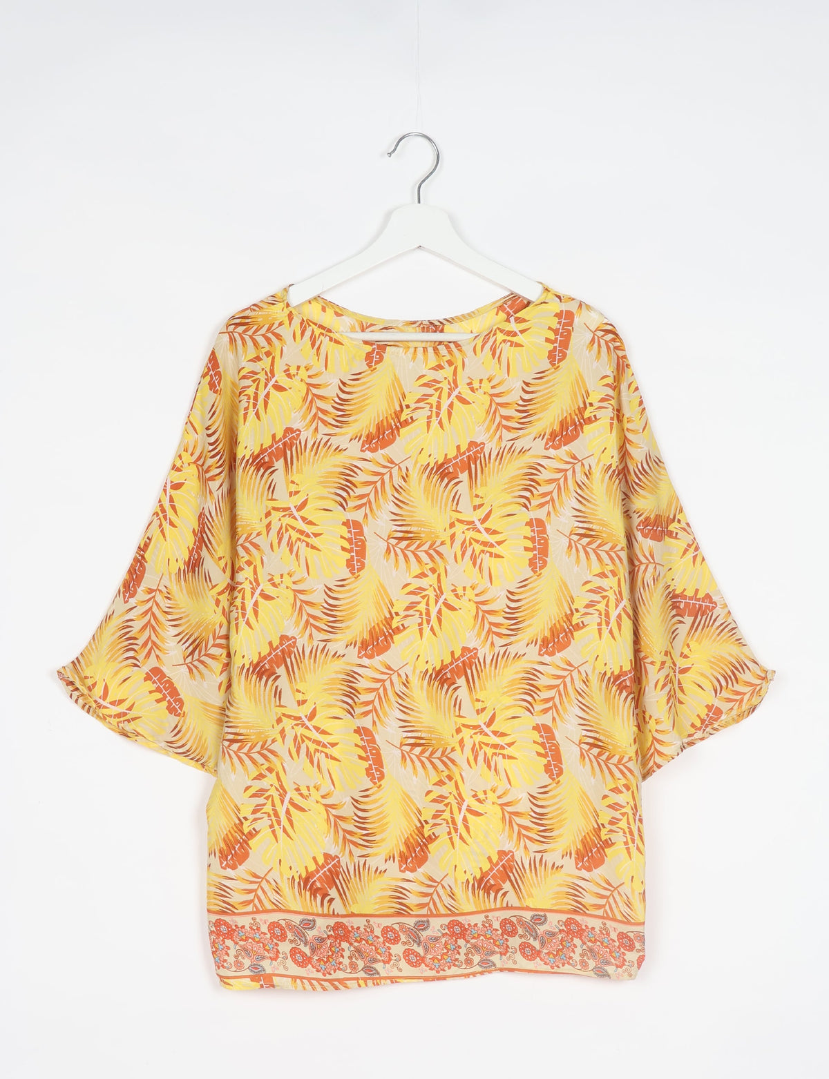 Yellow leaf-patterned belt top with wide sleeves and floral border hem, hanging on white hanger against white background