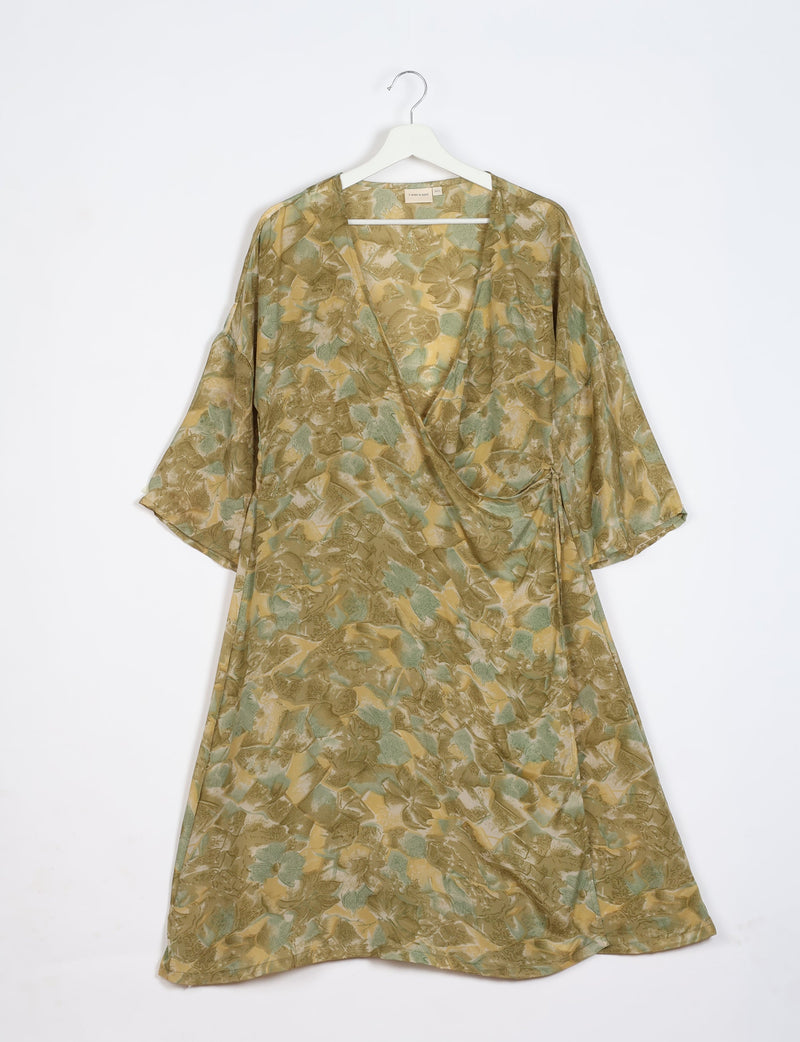 Green and beige abstract floral wrap dress with 3/4 sleeves hanging on white hanger against white background
