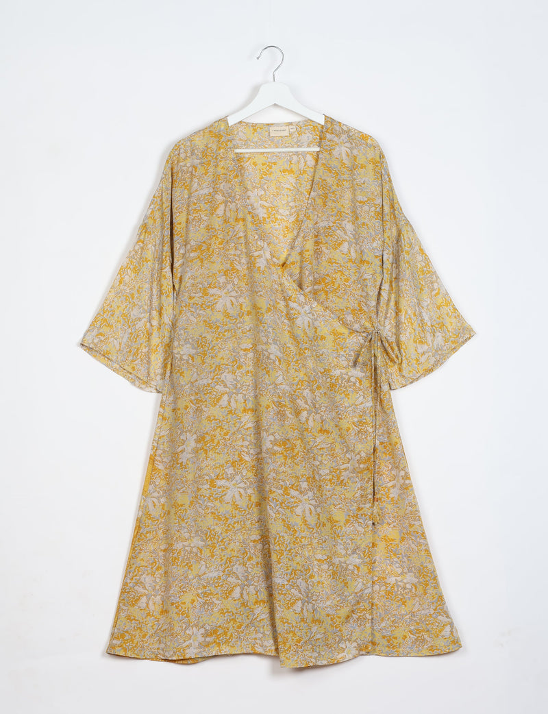 Yellow tropical floral wrap coat with wide sleeves hanging on white hanger against white background