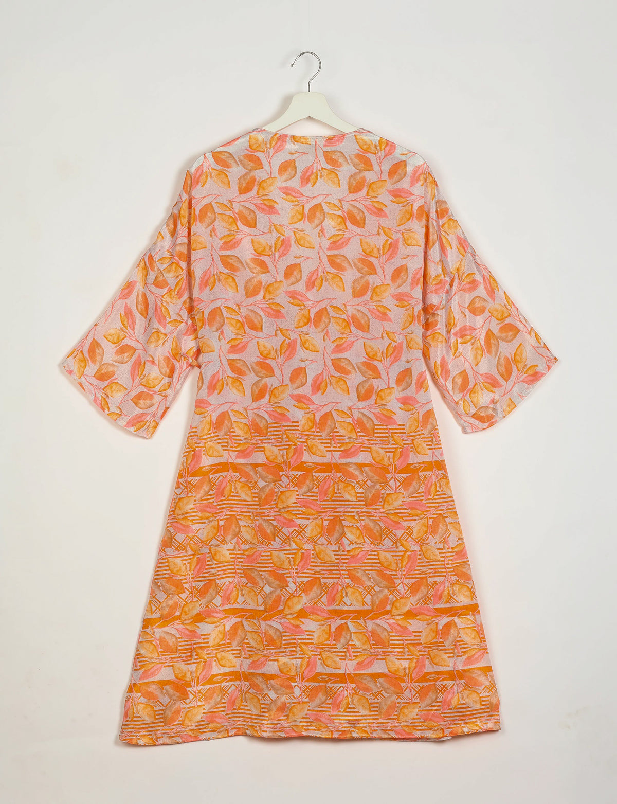 Orange and pink leaf-patterned coat with wide sleeves hanging on white hanger against white background