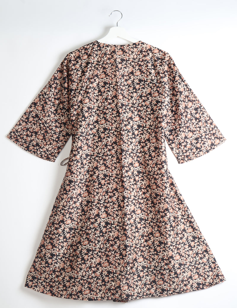 Black coat with beige and brown floral tropical print, wide sleeves, and a tie belt, shown from back on white hanger