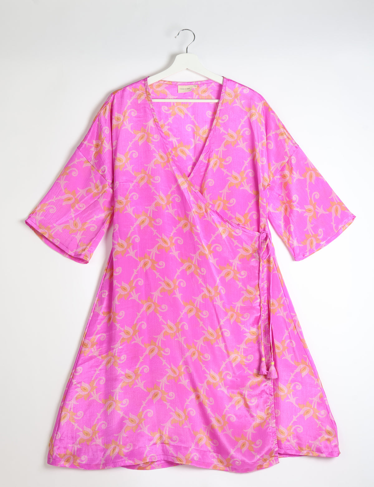 Pink floral wrap coat with wide sleeves and side tie, hanging on white hanger against white background
