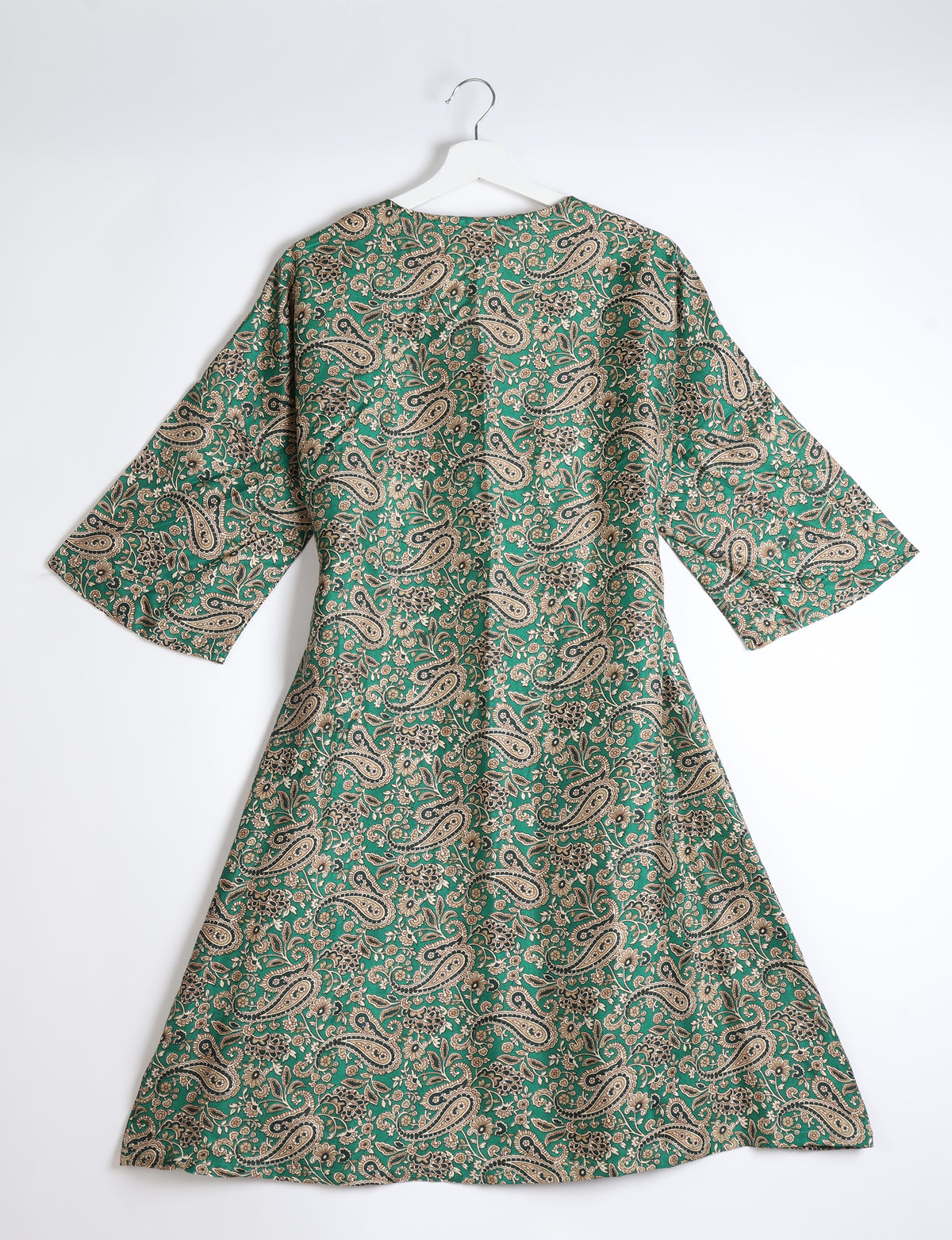 Green paisley patterned coat with wide sleeves hanging on white hanger against white background
