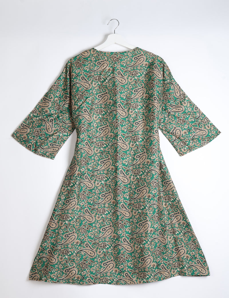 Green paisley patterned coat with wide sleeves hanging on white hanger against white background