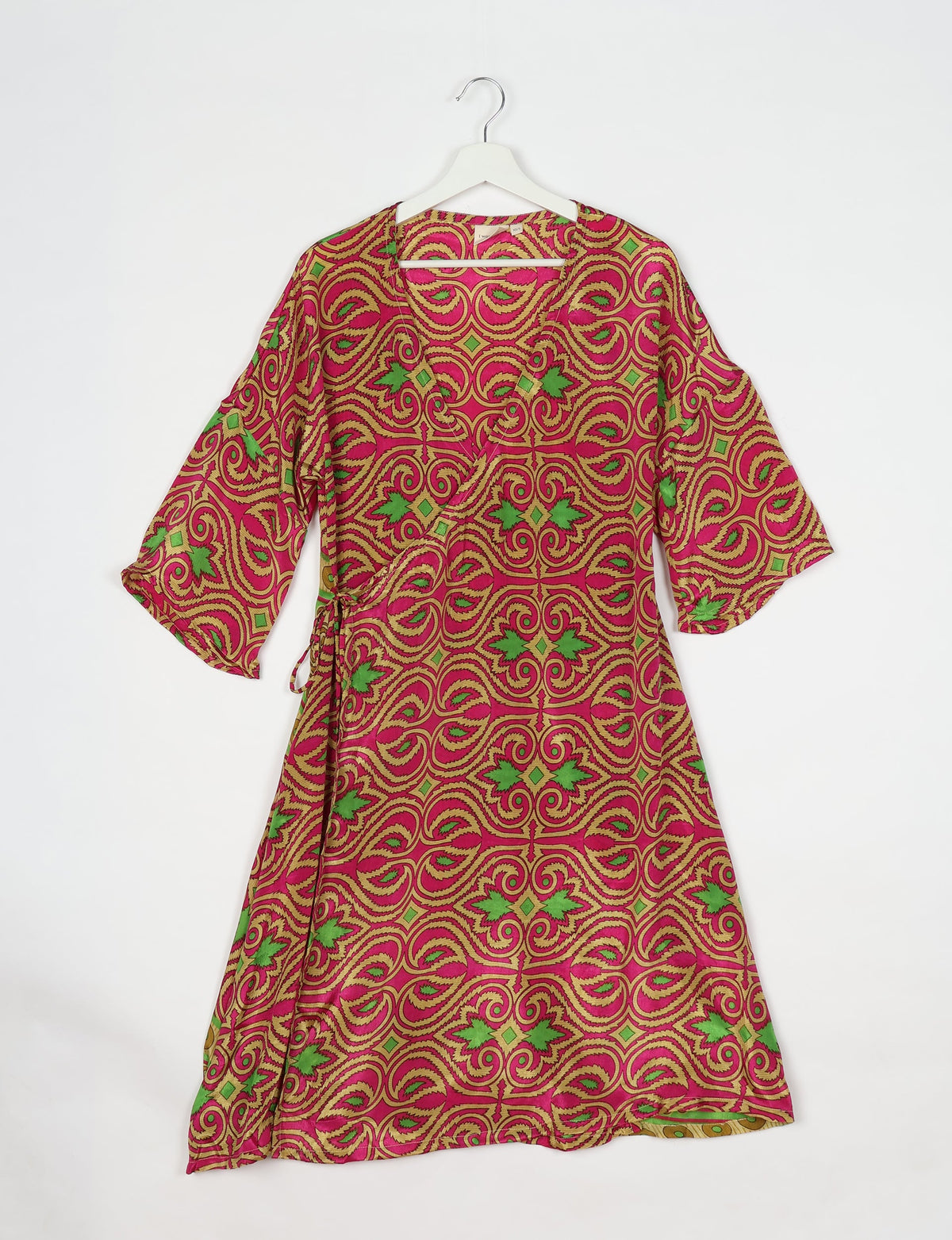 Pink paisley wrap coat with green and gold ornate swirl pattern, three-quarter sleeves, hanging on white hanger front view