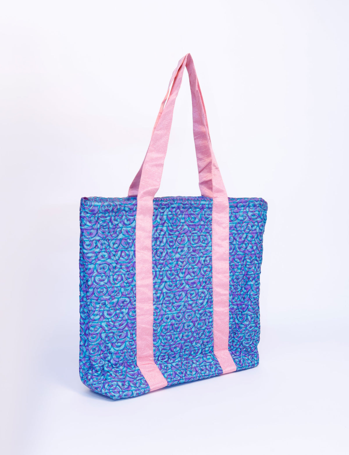 Quilted tote bag with blue abstract swirl pattern and long pink fabric handles, shown front side on white background