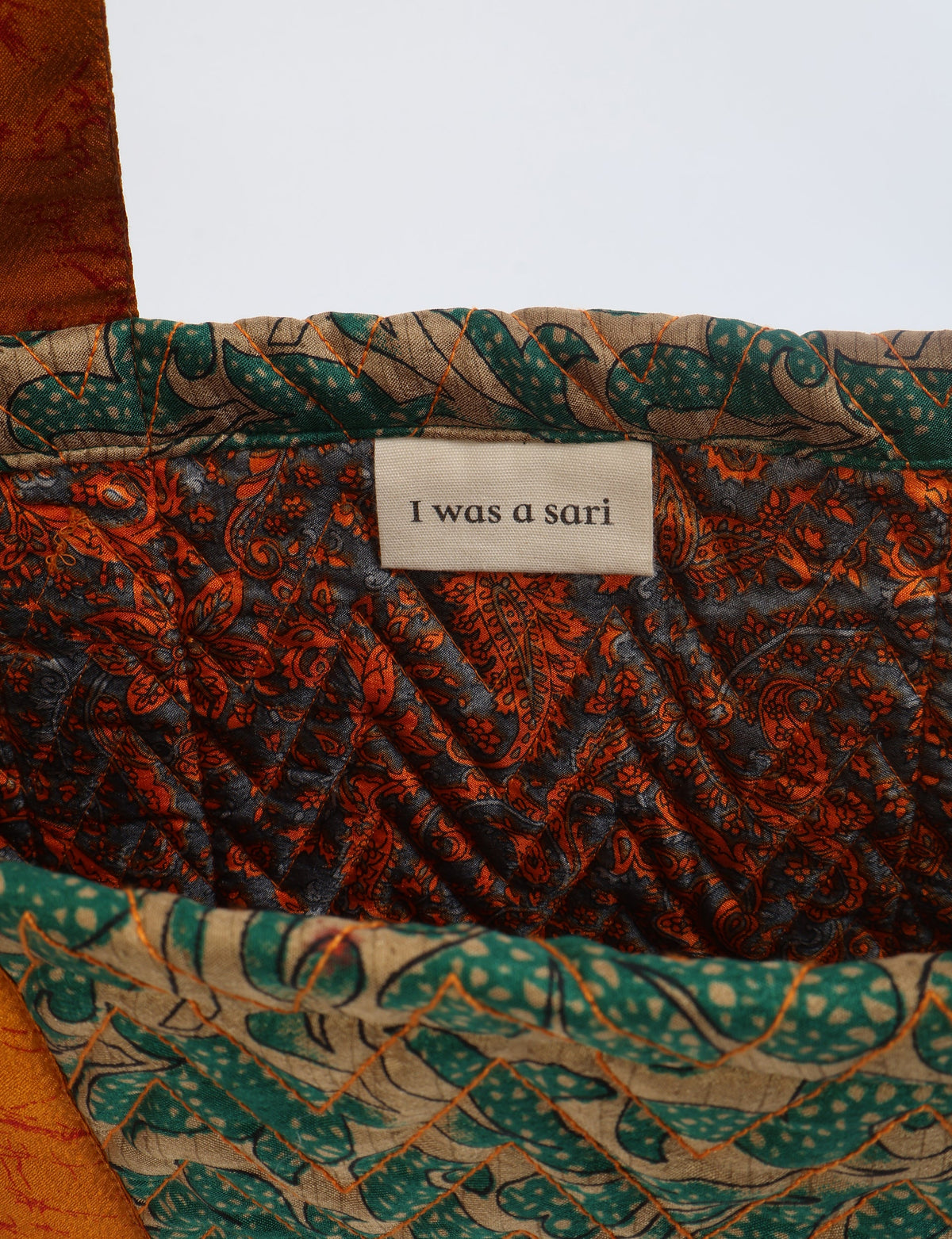 Quilted fabric tote bag interior with green and orange floral pattern and label reading "I was a sari"
