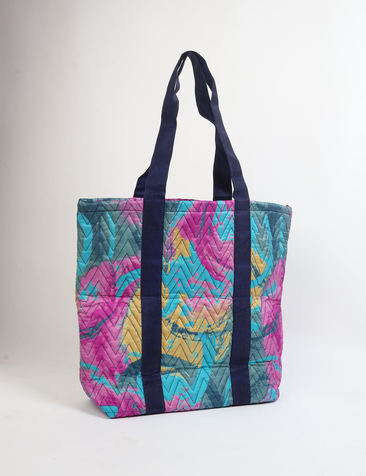 Quilted tote bag with pink, blue, yellow abstract zigzag pattern and dark blue vertical handles, front view, standing