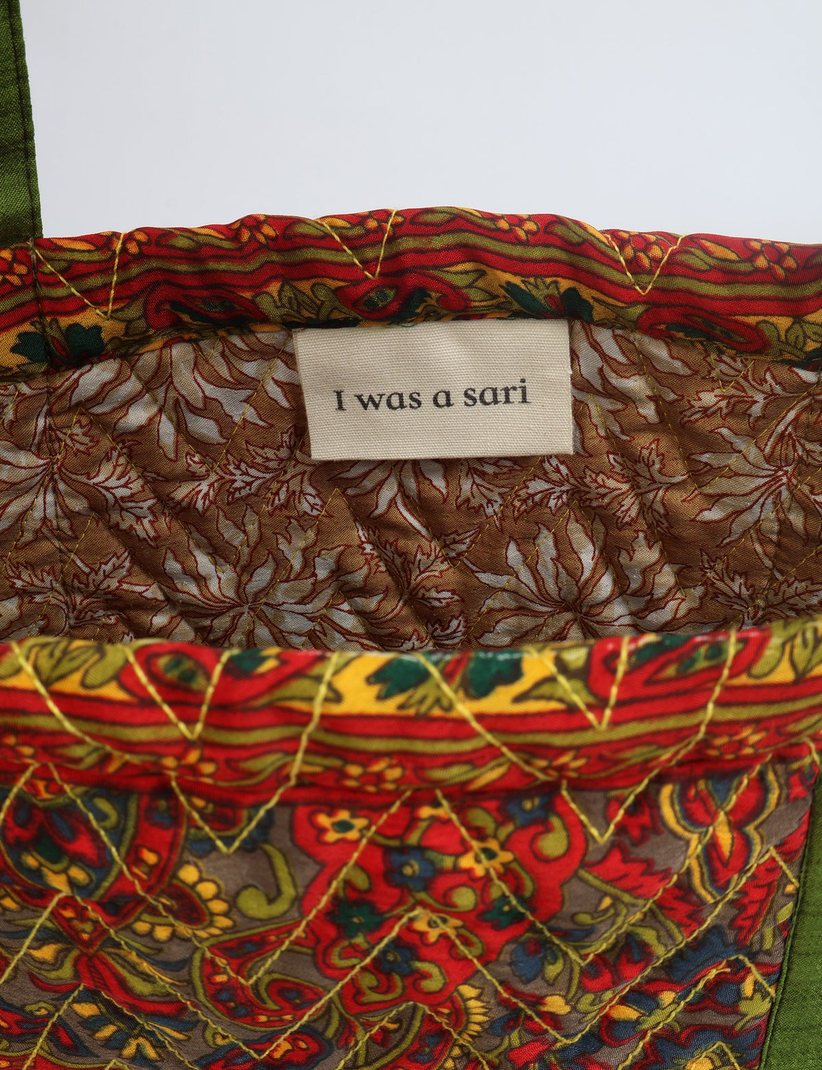 Quilted tote bag with red paisley pattern, green handles, and interior label reading "I was a sari"