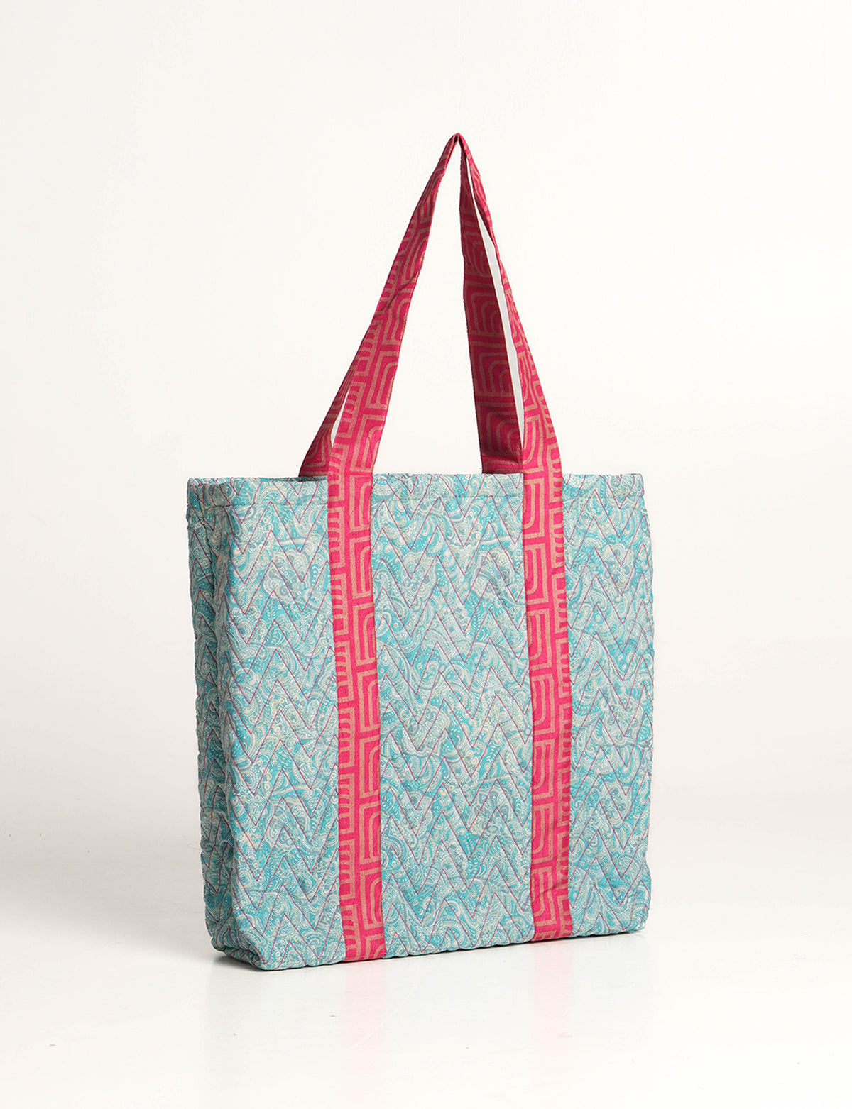 Quilted tote bag with blue zigzag pattern and pink geometric handles, shown in side view on white background