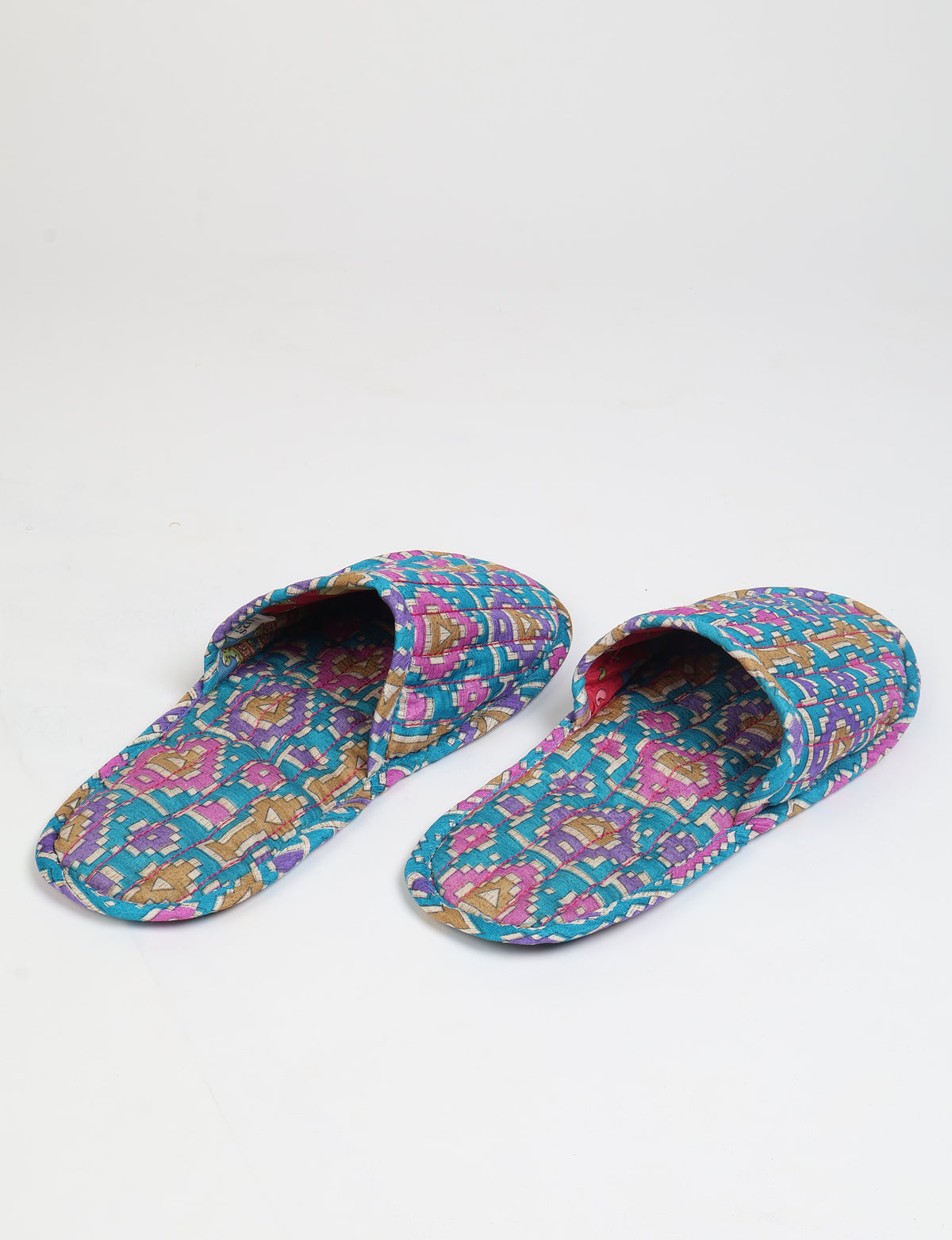 Pair of quilted slippers with blue, purple, and tan geometric pattern, shown from top front angle on white background