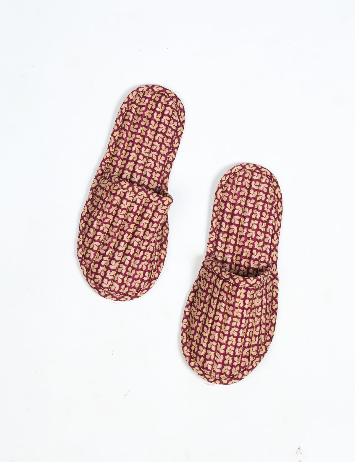 Quilted slippers with red and beige leaf pattern, top view, showing rounded toe and slip-on design on white background
