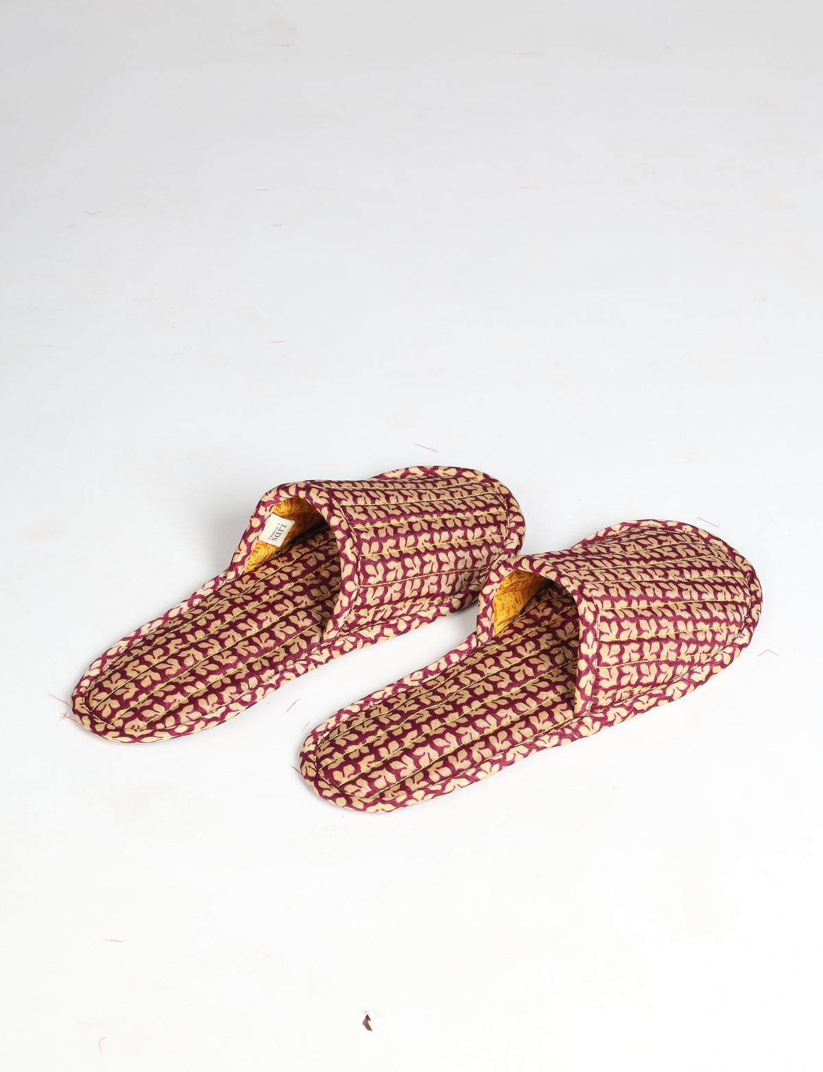 Pair of quilted slippers with red and beige leaf pattern, open back, and yellow inner lining, flat lay on white background