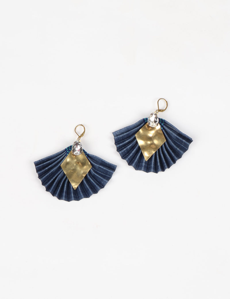 Pair of pleated blue fabric earrings with gold diamond-shaped metal accents and clear teardrop crystals, flat lay view
