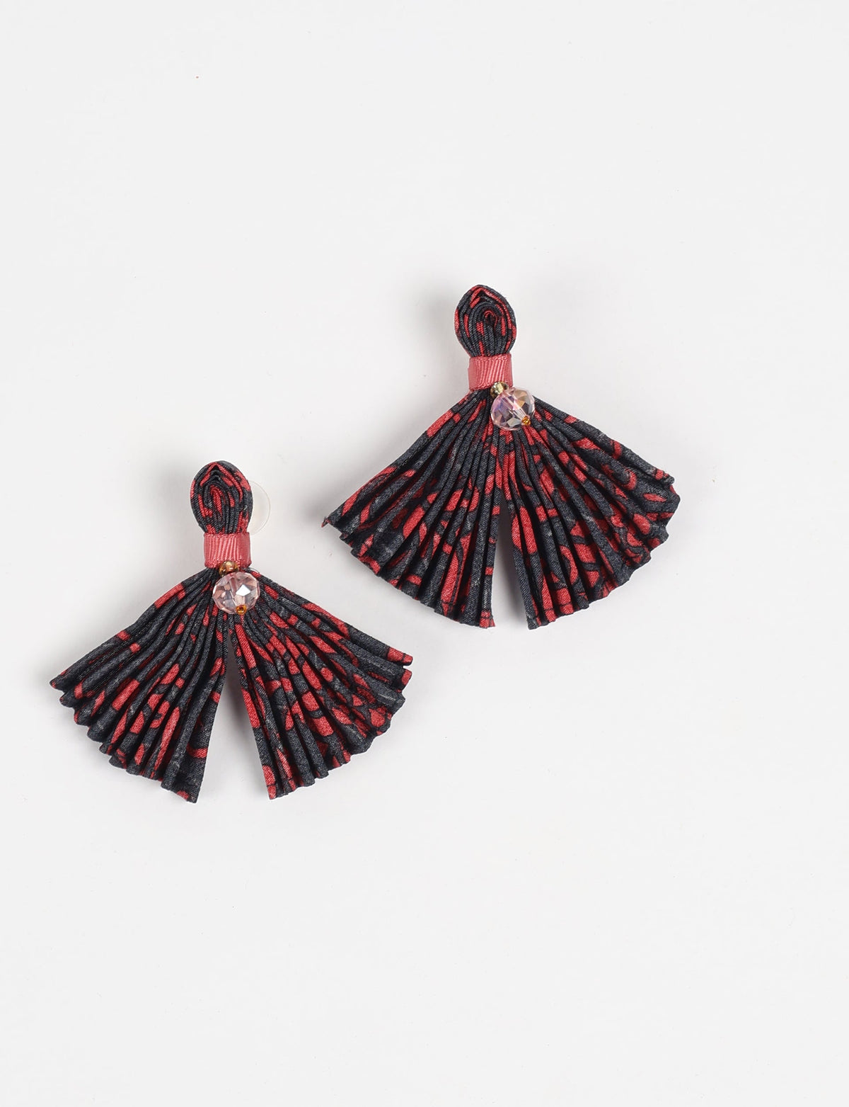 Pleated fabric earrings in black and red abstract pattern with pink ribbon and clear faceted bead, flat lay on white background