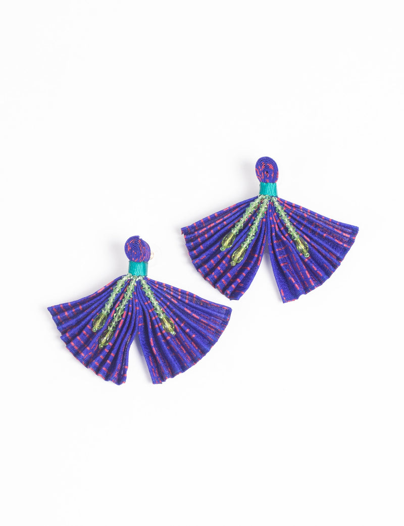 Pair of pleated earrings in blue with red dots, green bead accents, and green thread detail, flat lay on white background