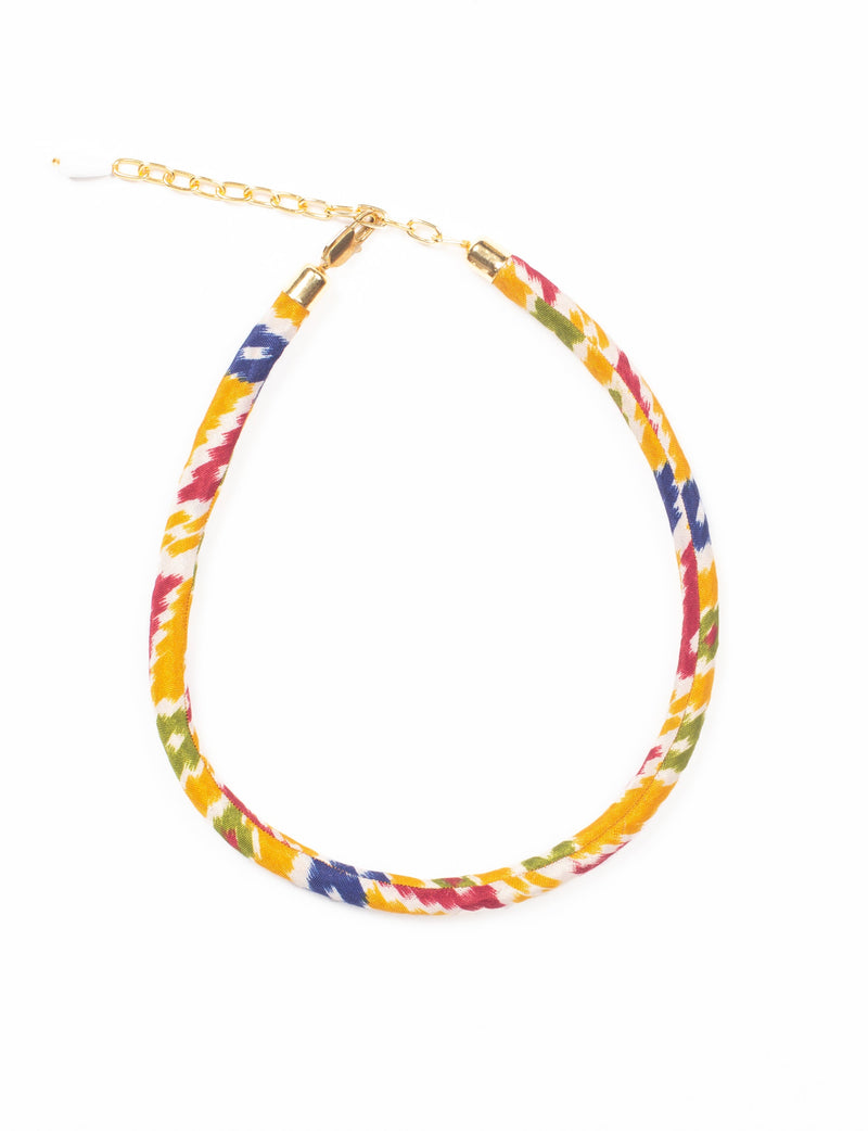 Rope necklace with yellow, red, blue, green, and white ikat fabric pattern and gold-tone chain clasp, flat lay view