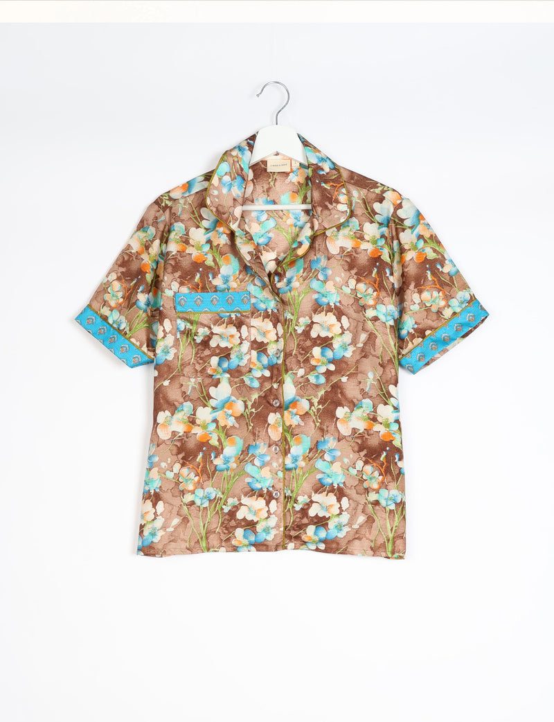 Brown short-sleeve pajama top with blue, white, and orange floral print and blue patterned trim on cuffs and pocket